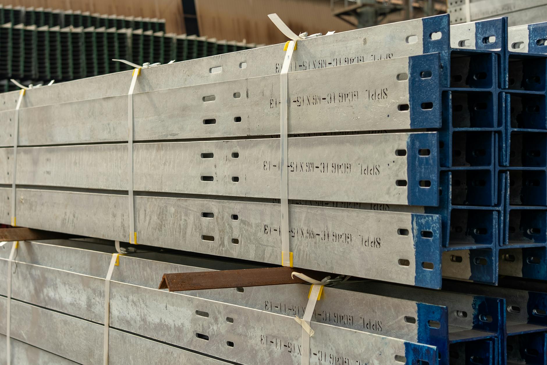 Close-up of stacked metal beams secured with straps in an industrial warehouse setting.