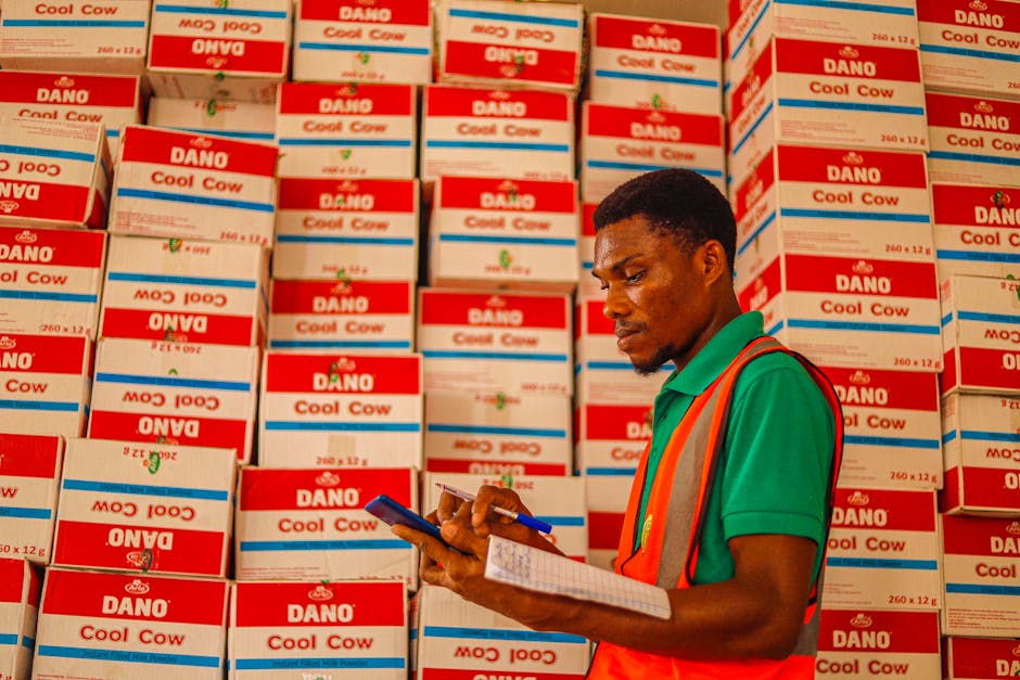Focused warehouse employee taking inventory notes amid stacks of Dano Cool Cow boxes.